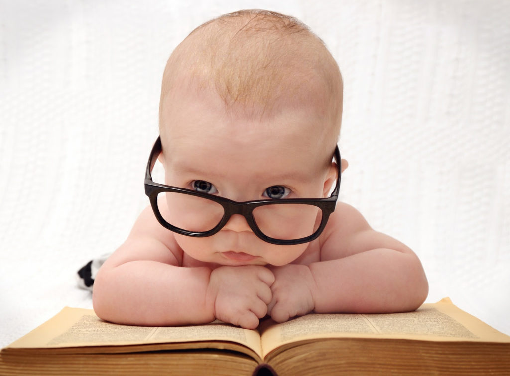 close-up of adorable baby in glasses lying on an old book and light background